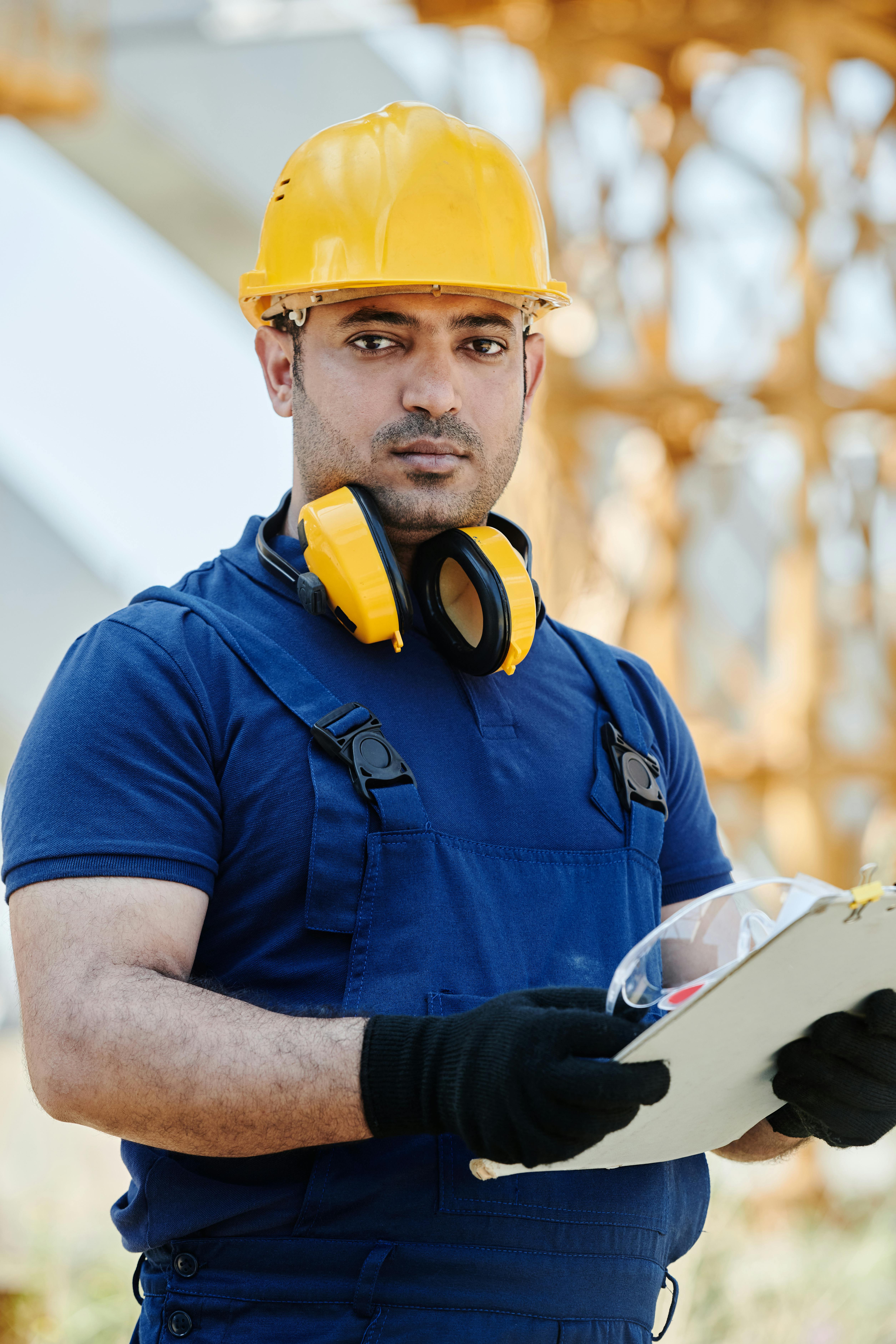Construction professional in safety gear holding a clipboard on an active worksite.